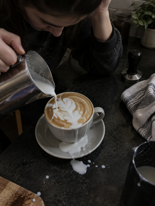 Amateur home barista messily hand-pouring latte art with milk spilled on the counter